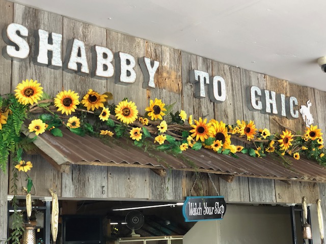 The Shabby To Chic antique store sign in Coffeyville, KS features a rustic wooden look highlighted with bright, cheerful sunflowers.